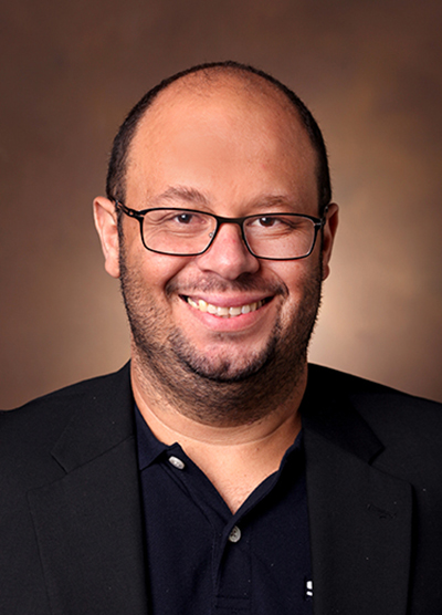 Headshot of Henrique Serezani wearing a black coat and eyeglasses.