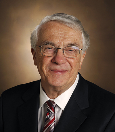 Headshot of Michael Waterman wearing a dark jacket and red-striped tie. He is wearing eye-glasses.