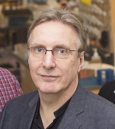 Headshot of Chris Wright. He's wearing a black dress shirt and a gray jacket over it.