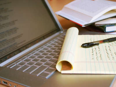 Close up of a laptop's keyboard with a legal pad and pen sitting on it.