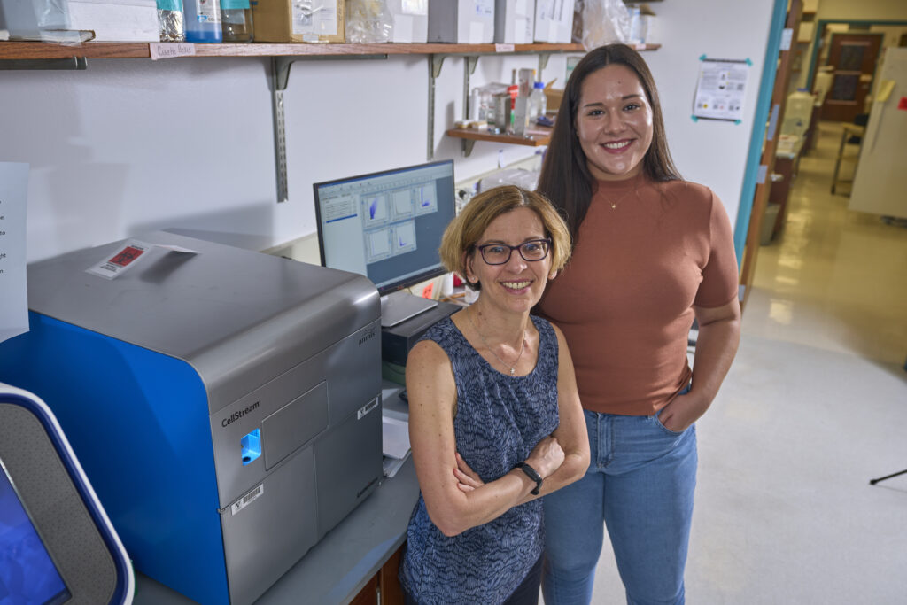 Alissa Weaver and Ariana von Lersner standing in front of a piece of lab equipment and a computer.