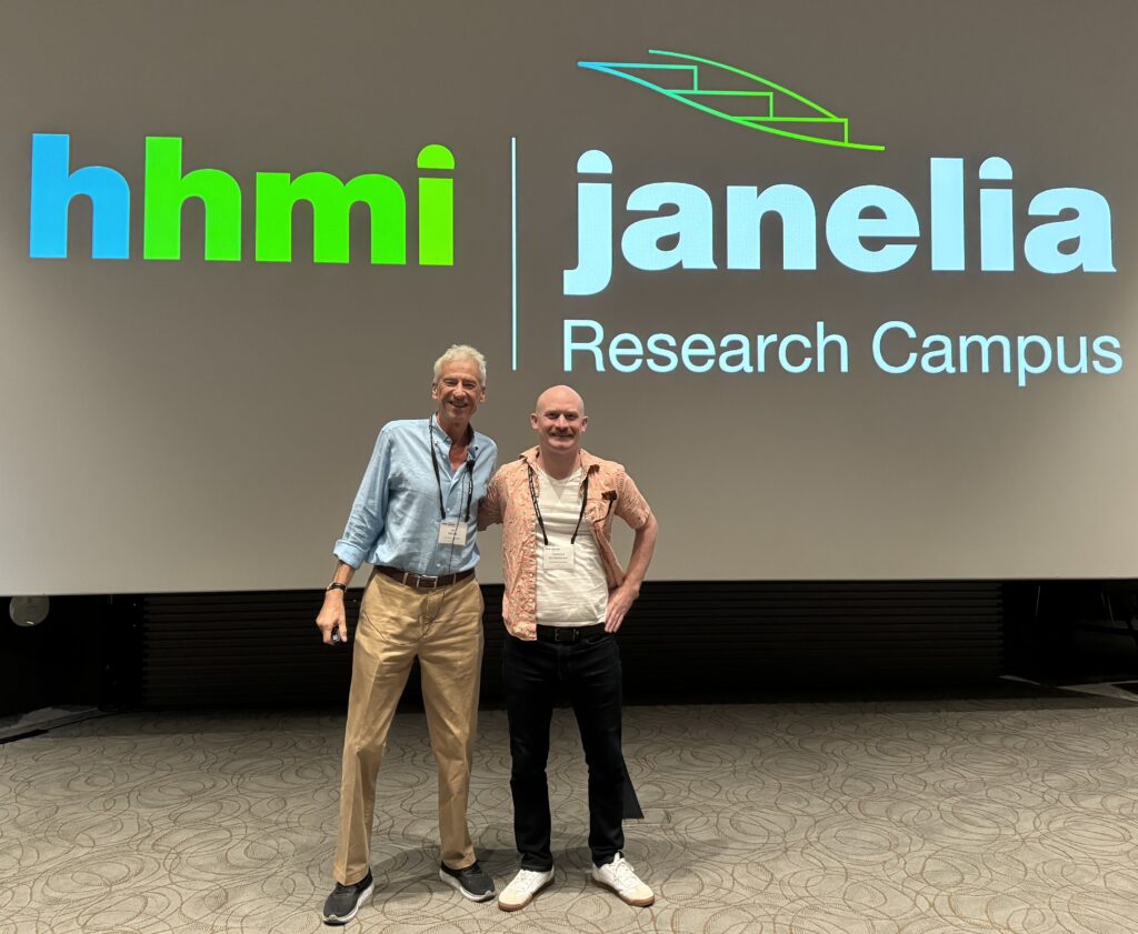 Macara and de Caestecker posing together at a conference. A screen behind them says "hhmi | janelia Research Campus."