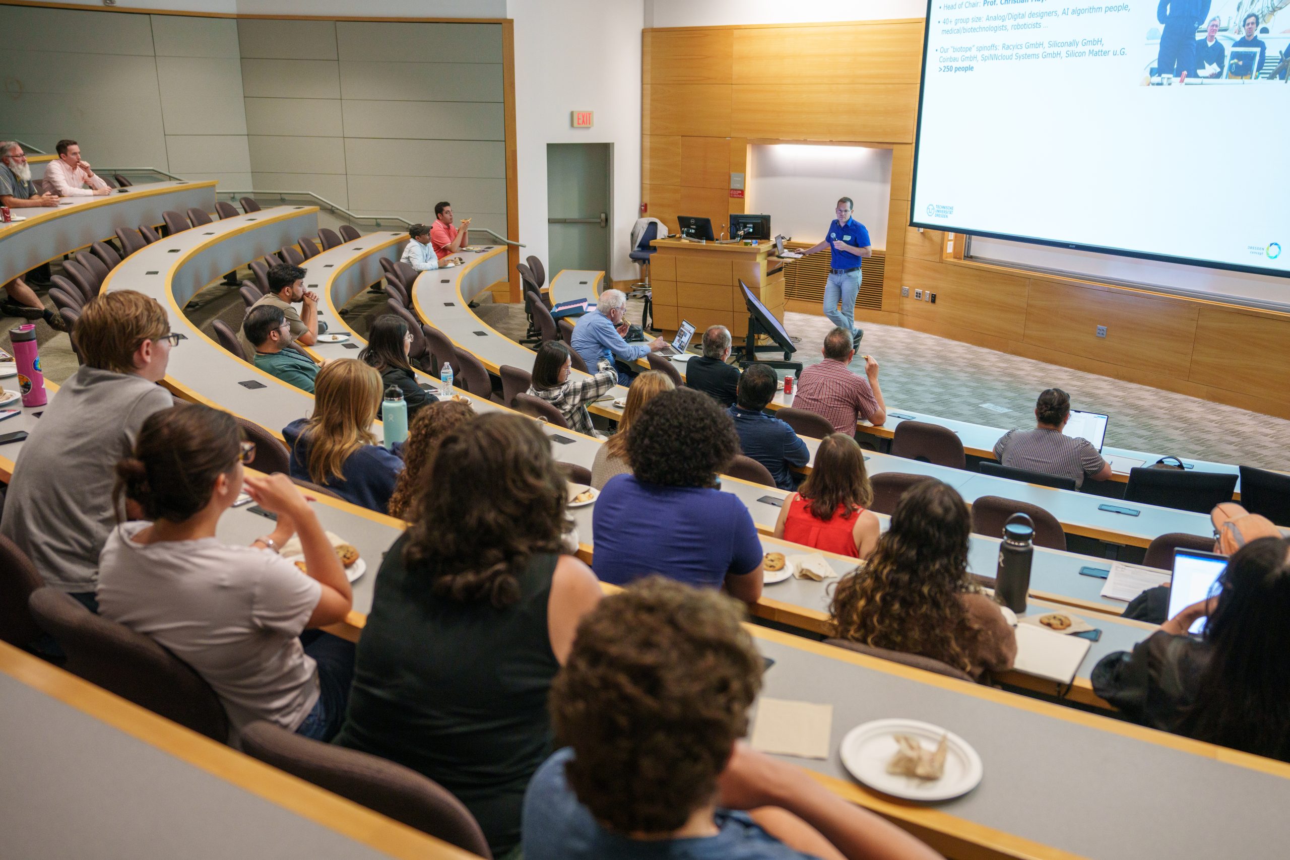 A person delivering a lecture at the front of a packed classroom.