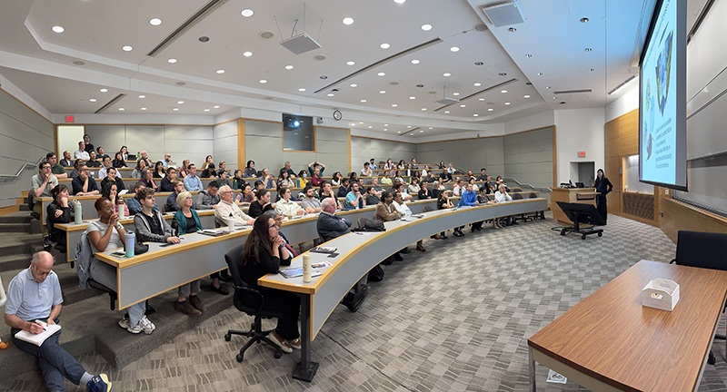 Photo of Jin Zhang at lecture (right) speaking to audience (left).