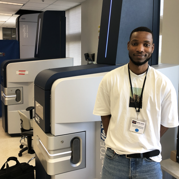 Photo of Sphamandla “Spha” Ntshangase standing near Bruker mass spectrometry instruments.