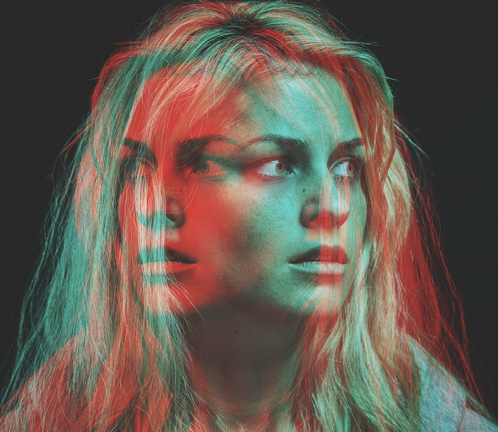 Two photos of a woman’s face overlaid on each other such that the woman is both looking left and right at the same time. The individual photos/layers are cyan and red. The woman’s expression is fearful.