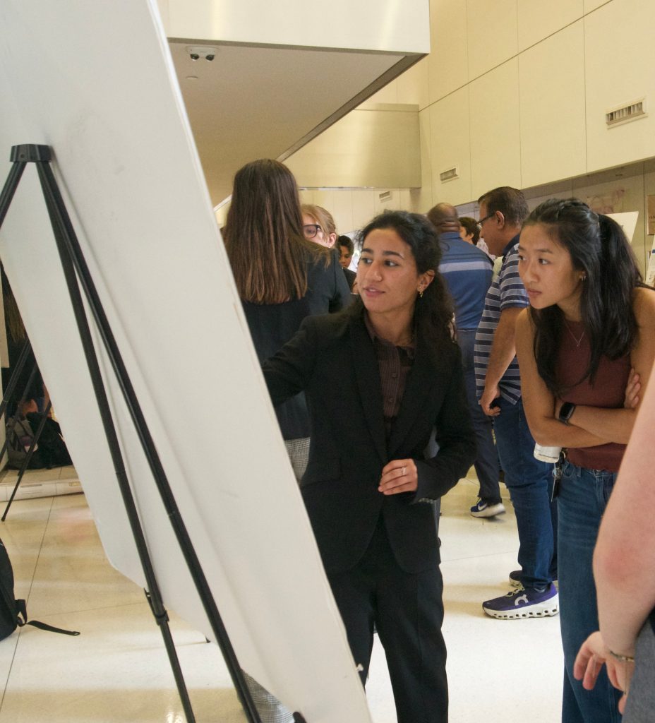 Two students discuss the contents of a research poster. The photo is taken partly from behind the poster.