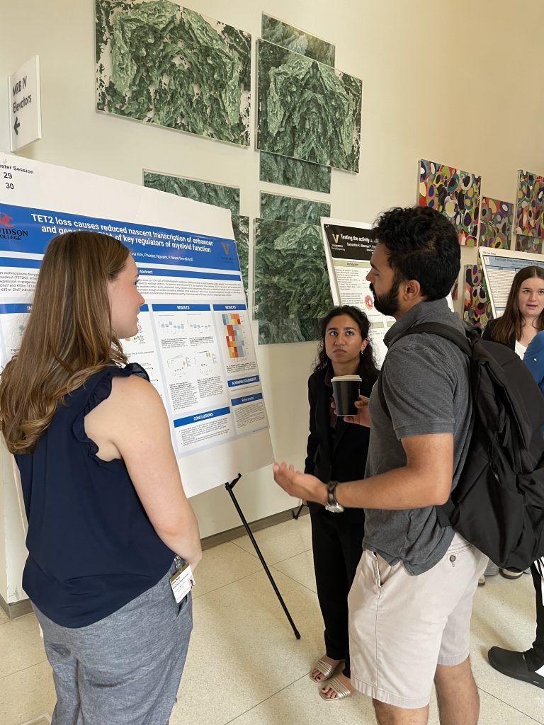 Three students talk in front of a research poster.