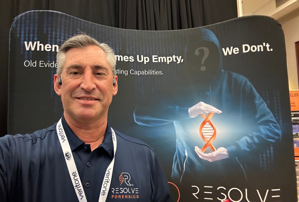 Selfie of Dave Vigerust in a Resolve Forensics–branded shirt posing in front of a Resolve Forensics–branded banner at a conference.