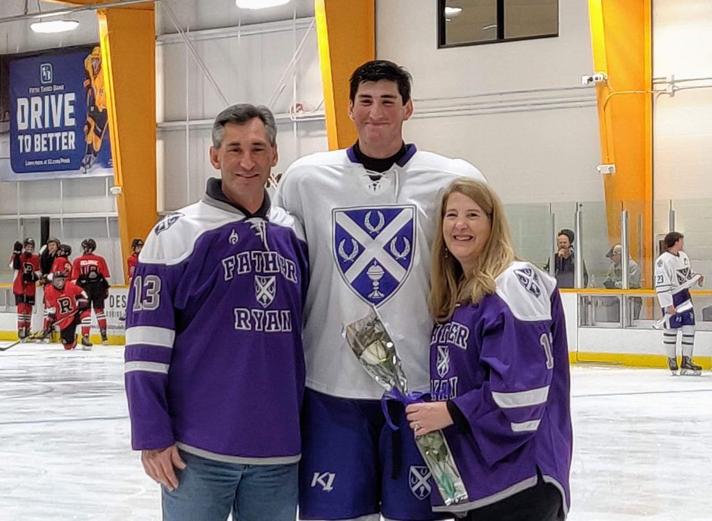 Dave Vigerust, left, with his son, middle, and a woman. The son is wearing a white hockey jersey and the man and woman are wearing purple "Father Ryan" hockey jerseys.
