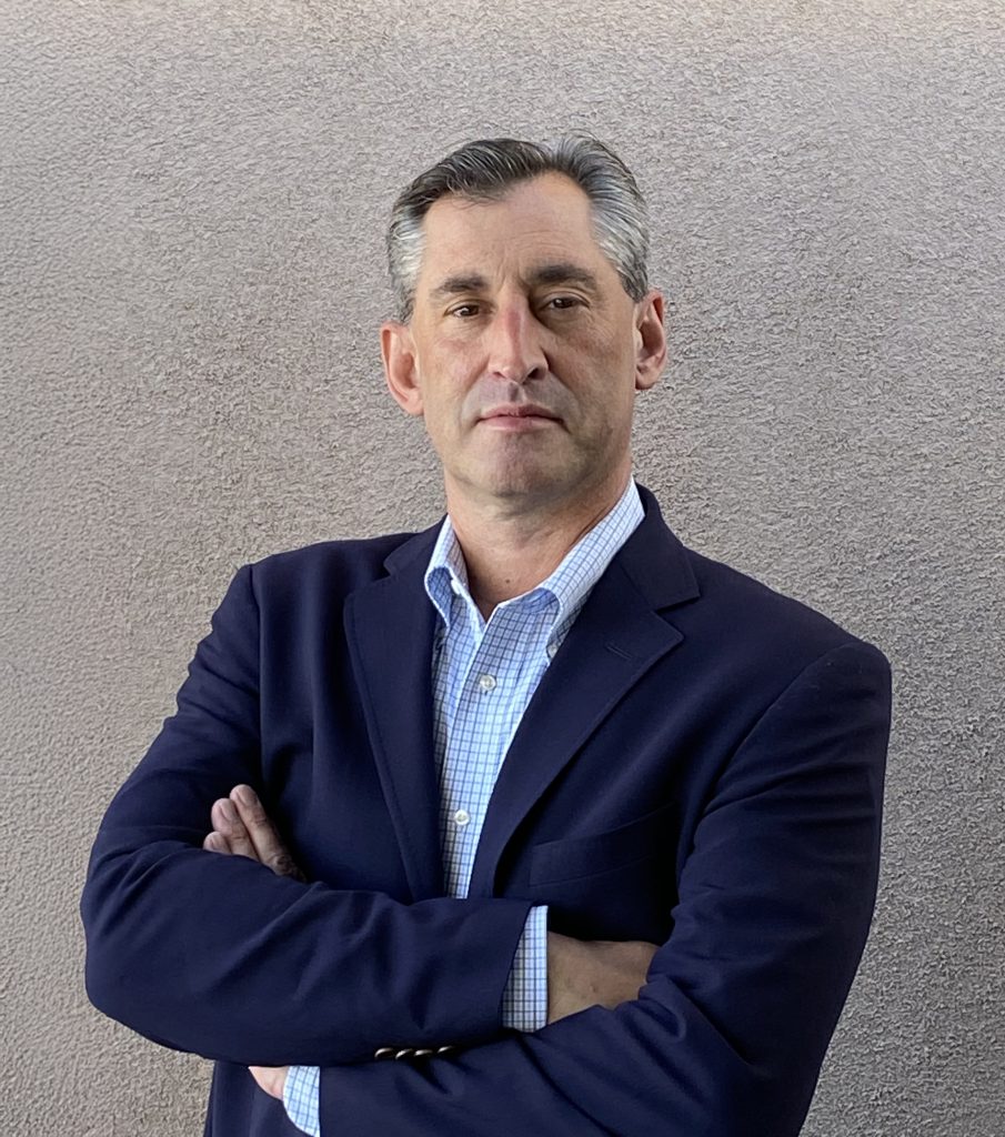Headshot of Dave Vigerust in a navy suit on a gray background