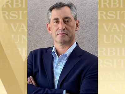 Headshot of Dave Vigerust in a navy suit on a gray background. The image is overlaid over a golden background emblazoned with the Vanderbilt name.