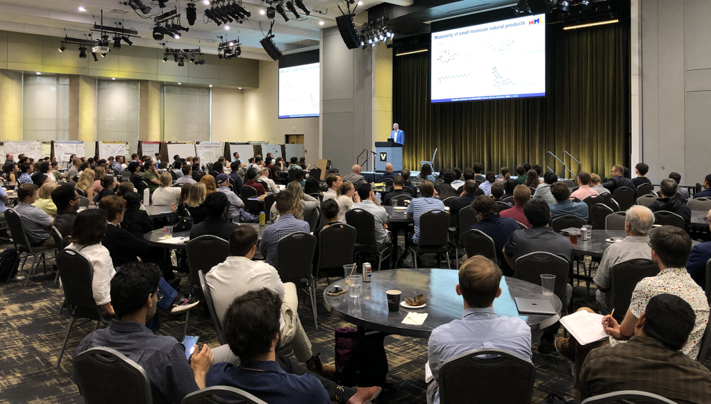 Photo of people sitting a tables at a symposium.