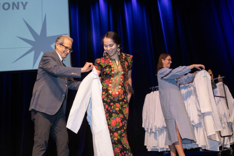 Photo of man putting a lab coat on a graduate student.