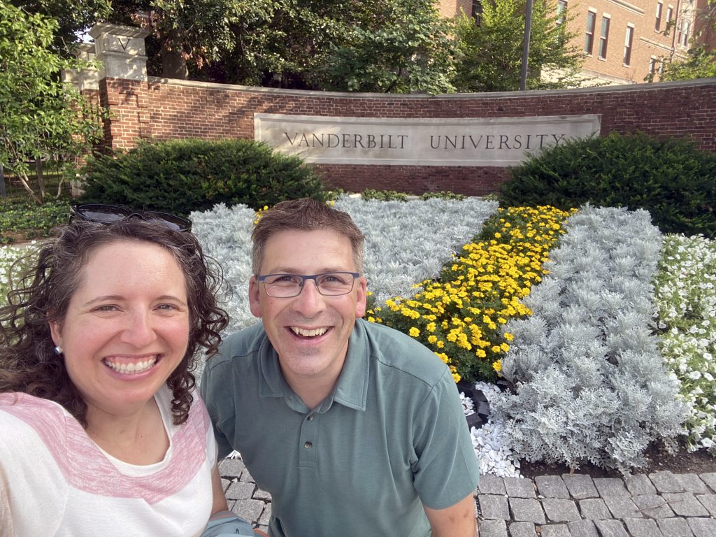 Selfie of Chrystal, left, and Hans Sohl in front of a wall on campus that says “Vanderbilt University” and has flowers planted in front of it.
