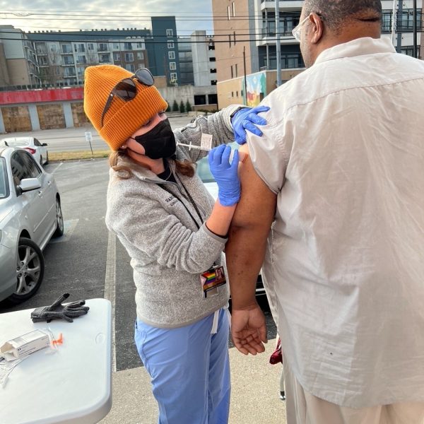 A woman in scrubs and a sweater gives a vaccine to a person wearing a white shirt