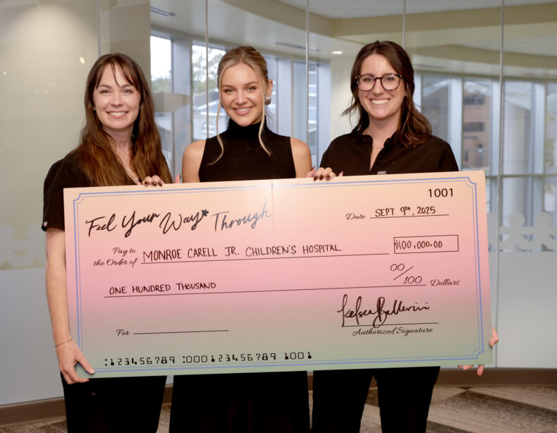 Three women hold an oversized donation check.