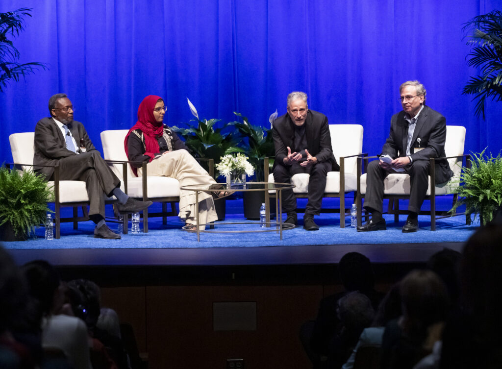 Two physicians and a medical student sit on stage with comedian and advocate Jon Stewart