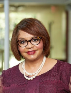 A woman wearing glasses smiles in an atrium area