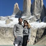 Two people in gray fleeces stand in front of a snowy mountain