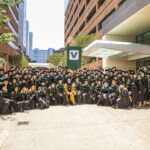 MD Class of 2022 stands outside in their doctoral regalia with Dean Balser. VUMC buildings surround them.