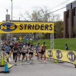 Runners cross the starting line below a Nashville Striders banner