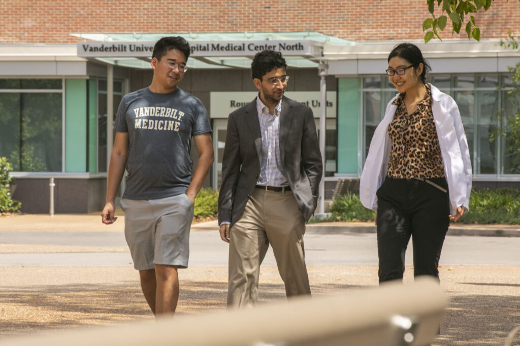 Two men and one woman in a white coat walk along a medical center plaza.