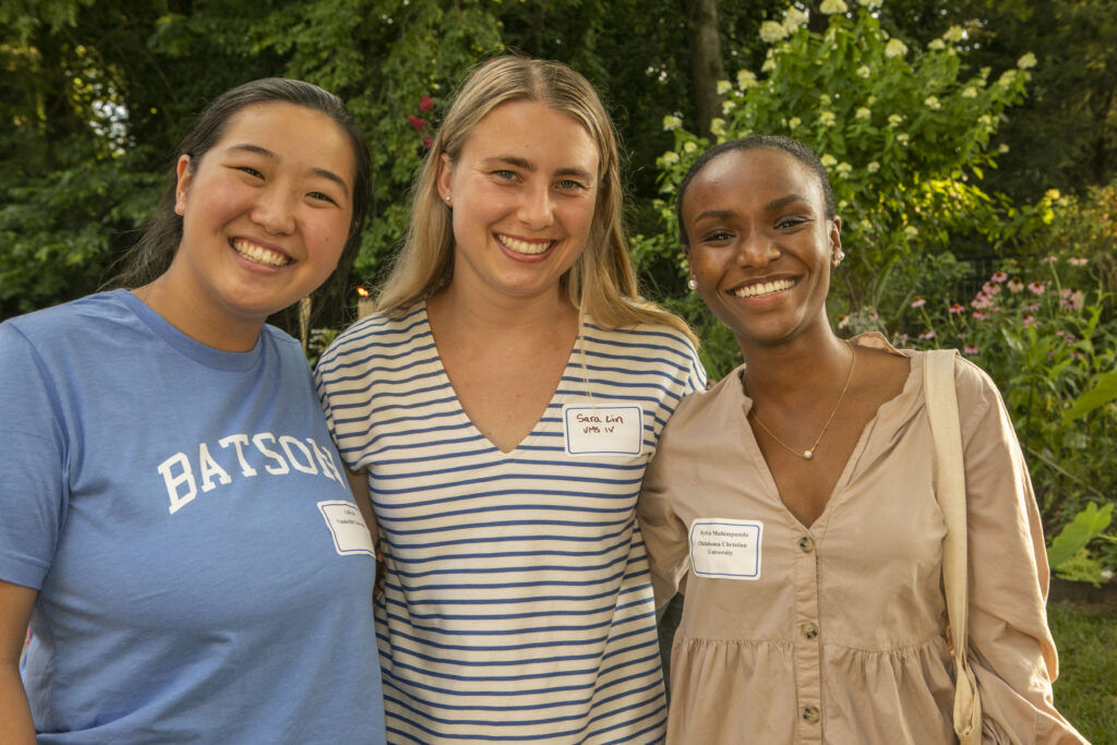 Three women pose for a photo outside. They all smile.