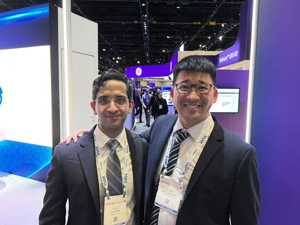 Two men in suits, ties, and lanyards stand in the middle of a conference hall