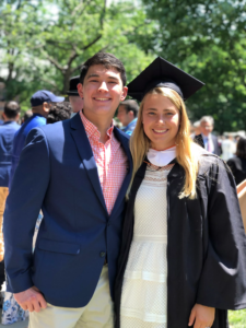 A graduate with a master's hood stands with a man in a button down and blazer