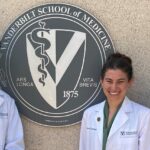 Three medical students in white coats stand next to a medical school seal