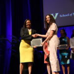 A dean in a yellow dress presents an award to an MD student