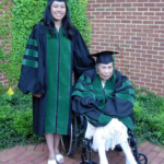 A female medical school graduate poses with her grandmother while both wear academic regalia.