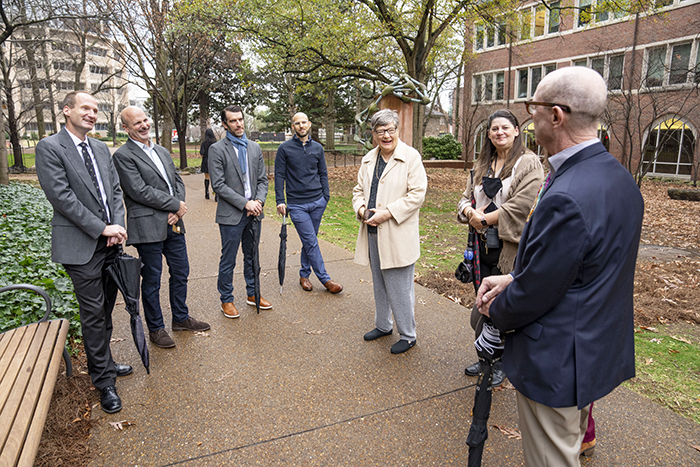 Phot of (L-R) David Cortez leaning on an umbrella, John York with hands folded, Taylor Wood holding an umbrella, Aaron Conley leaning on an umbrella, Jan Jordan wearing a cream-colored coat, Jen Smith wearing a brown sweater, and Larry Marnett wearing a blue blazer and holding an umbrella.