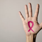 A human hand, palm open to the viewer, with a pink ribbon drawn on it. The pink ribbon is the chosen symbol for breast cancer awareness.