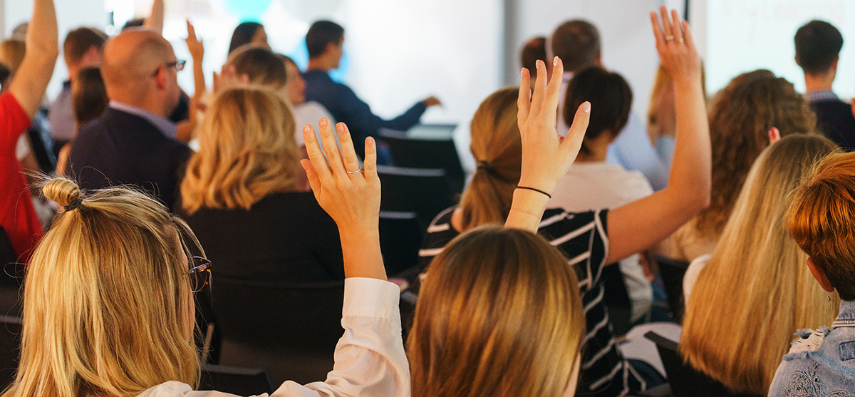 Participants of the conference vote and signal the speaker with their hands up in a special audience with a projector and screen. Education and training of employees. Soft focus and beautiful bokeh.