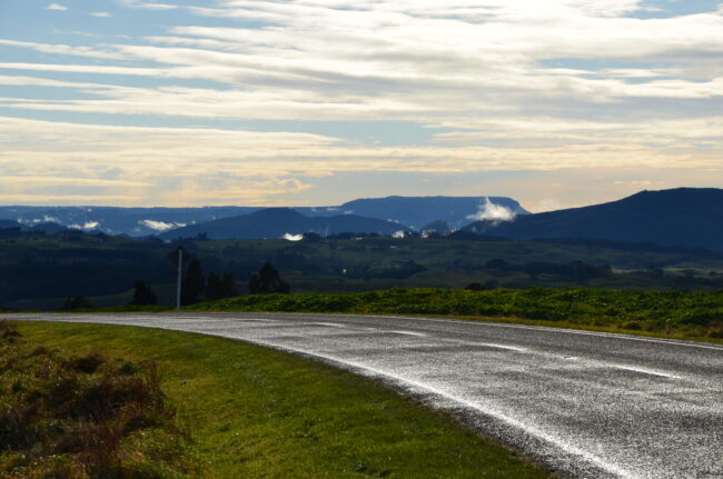 Asphalt road with a series of grassy mountains in the distance at sunset