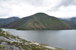 View of cloudy skies and a lake overlooking grassy mountains in the distance