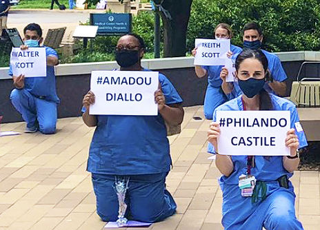 VUMC workers kneel while holding BLM signs.