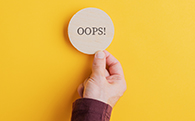 Male hand placing wooden cut circle with an Oops sign on it on bright yellow background.