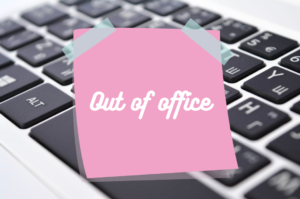 image of a laptop keyboard with a pink post it note on it that says Out of Office