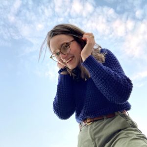 Picture of Chloe Hall wearing glasses and a blue sweater with the blue sky in the background.