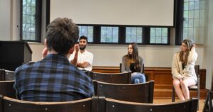 This image from the 2023 Undergraduate Creative Writing Symposium features three panelist in the background and the back of an audience member in the foreground.