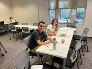 This image depicts a Writing Studio writing consultation between a male-presenting student and a female-presenting student in the Writing Studio's space.