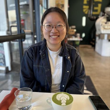 Asian woman with glasses smiles over a cup of coffee