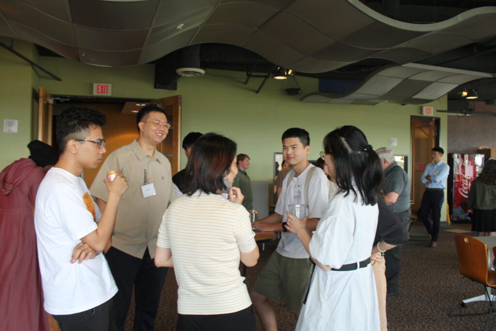 Five people in foreground chatting around a table while more socialize in background