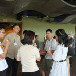 Five people in foreground chatting around a table while more socialize in background