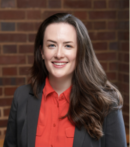 Headshot of Jessica Lowe. Subject is wearing professional dress and standing before a brick wall.