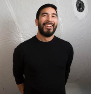 Headshot of Alejandro Acierto wearing black and standing in front of a white background.