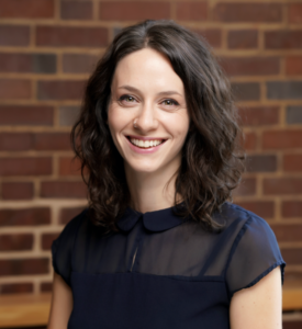 Headshot of Jennifer Gutman. Subject is wearing professional dress and standing in front of a brick wall.